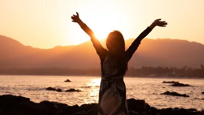 Woman with arms outstretched on beach showing positive attitude - Photo by Bai Z on Unsplash