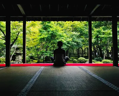 Person meditating beside calm water, framed by traditional architecture