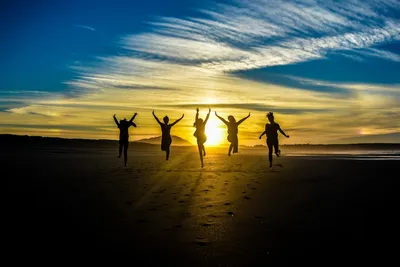 People jumping in celebration on beach at sunset — Photo by Guille Álvarez on Unsplash