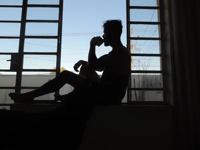 Silhouette of a person drinking coffee by the window, embracing the peaceful early morning solitude. Photo by Victor Caldas on Unsplash