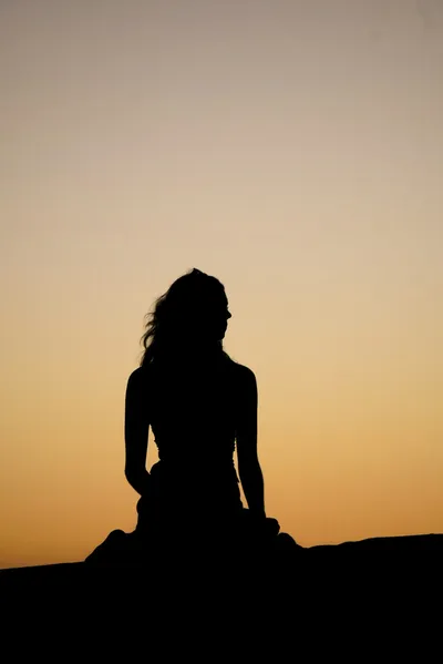 Silhouette of a woman against a sunset sky, symbolizing the peaceful mindset of intentional living. Photo by Naveen Ketterer on Unsplash